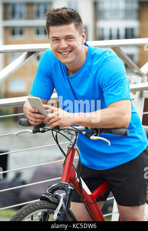 Young Man Using Mobile Phone Whilst Out On Cycle Ride In Urban Setting Stock Photo