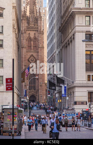 Tourists and business people walk down Wall Street with Trinity Church beyond, New York City, USA Stock Photo