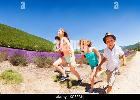 Portrait of happy age-diverse boys and girls running together through lavender field at sunny day Stock Photo