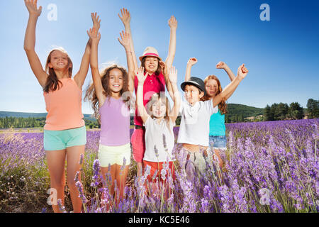 Portrait of six happy boys and girls standing together in lavender field with their hands up Stock Photo