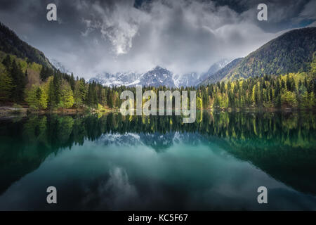 Panoramic view of Fusine Lake, in Italian Alps, near Slovenia. Cloudy, daylight. Snow in the mountains. Mirror reflection on the water. Stock Photo