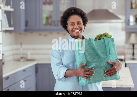 Smiling young African woman standing in her kitchen with groceries Stock Photo