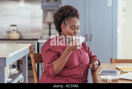 Young woman using a tablet and drinking coffee at home Stock Photo