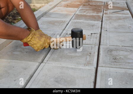 Man with a rubber mallet taps tiles on a pathway as part of a DIY construction project at home Stock Photo