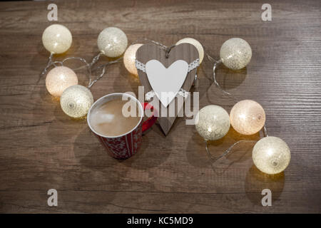 Decorative handmade heart, cup of coffee with multicolour lights on the wooden table Stock Photo