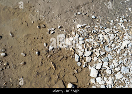 Murky dirty water from a muddy puddle recedes from the edge of stone pebbles as it evaporates due to the heat Stock Photo