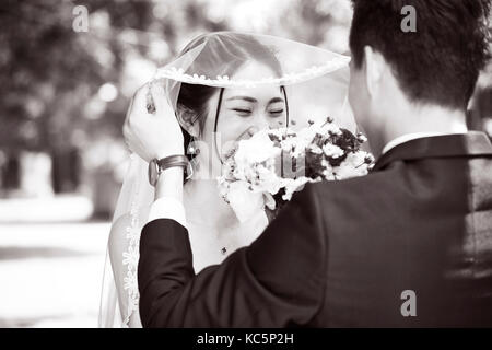 asian groom lifting up bridal veil to kiss beautiful bride, black and white. Stock Photo