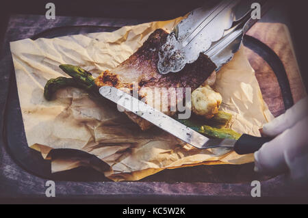 Process of cooking fish. hands cooks in clean white gloves puts grilled the fish on the paper lying on the Board. Stock Photo