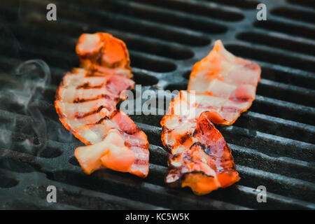 Grilled bacon skewers on a black background. Delicious strips of fatty ham on a hot grill. The ingredients for the sandwich. English Breakfast Stock Photo