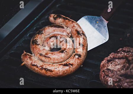 Grilled sausage with fresh rosemary on hot barbecue dish. the cook turns the frankfurter on the grill. Ingredients for hot dog, for Burger Stock Photo