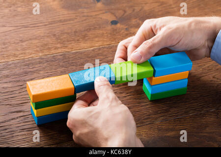 Person Hand Building Bridge Colorful Blocks At Wooden Desk