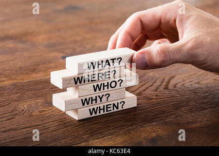 Person Arranging A Set Of Questions On Wooden Block At Wooden Desk Stock Photo