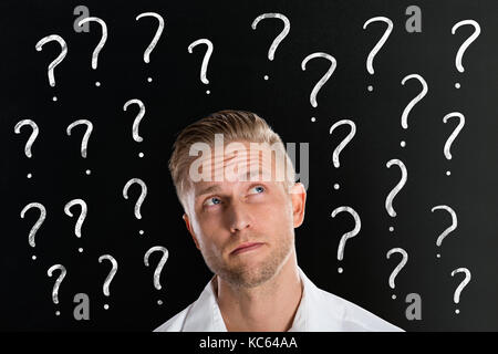Thinking Young Man In Front Of Question Marks Drawn On Blackboard Stock Photo