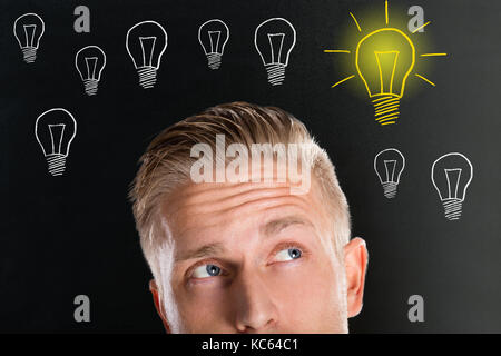 Handsome Thinking Young Man Looking Up With Creative Light Bulb Sketches On Black Board Stock Photo