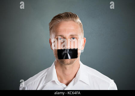 Young Man With Black Duct Tape Over His Mouth Against Grey Background Stock Photo