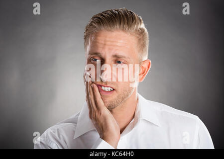 Young Man Suffering From Toothache Against Grey Background Stock Photo