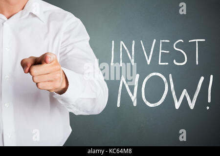 Invest Now Text With Business Man Pointing Toward Camera Stock Photo