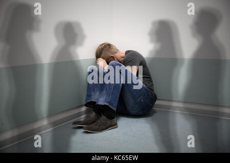 Scared Man Sitting In The Corner Of A Room With People Shadows On Wall Stock Photo