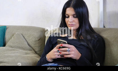 Attractive young woman using cell phone on couch Stock Photo