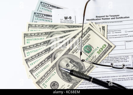 Close up image of money,$100 bills,W-9 form,glasses and a pen on white background Stock Photo