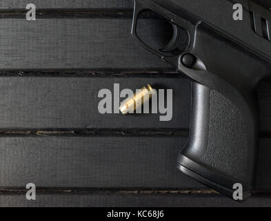 Polymer pistol and .45 caliber round on a black wooden surface, closeup, showing trigger and textured grip Stock Photo