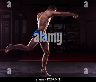 A male MMA fighter training kicks and punches in a dark gym Stock Photo