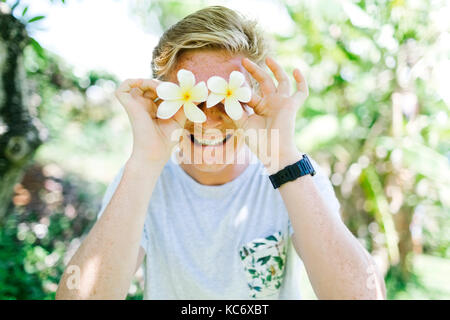 Portrait of young man holding gardenia flowers in front of eyes Stock Photo