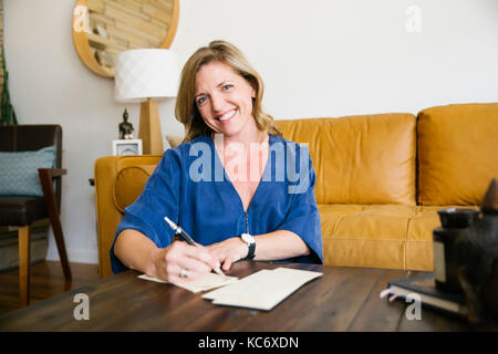 Portrait of woman writing letter in living room Stock Photo