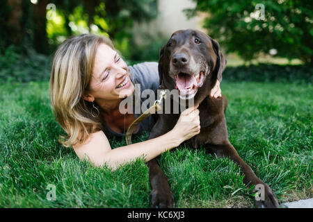 Smiling woman lying on grass with Labrador Retriever Stock Photo