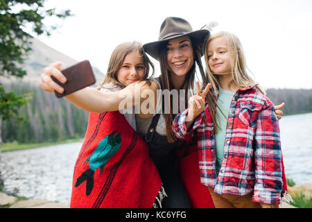 Outdoor portrait of mother with kids (6-7, 8-9) taking selfie by lake Stock Photo