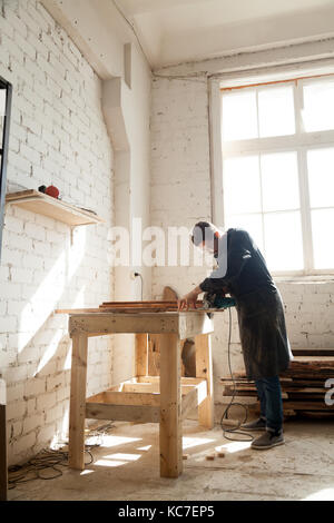 Skilled professional carpenter concentrated on work using electric tool in woodshop interior, cutting wood with power hand saw, craftsman making custo Stock Photo