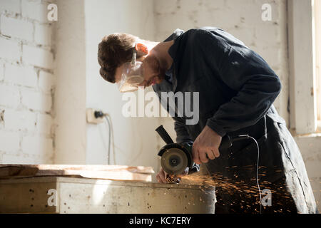 Side view of worker using angle grinder for metal cutting  Stock Photo