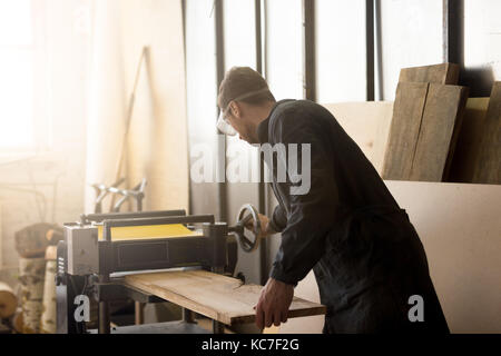 Worker operating stationary power planer, processing wooden boar Stock Photo