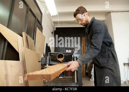 Skilled worker processing wooden flooring plank on woodworking p Stock Photo