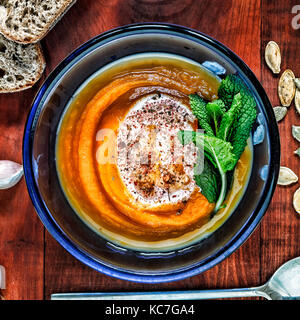 Roasted pumpkin and carrot soup with cream and pumpkin seeds on brown wooden background. Copy space.  Thanksgiving Day. Autumn. Stock Photo