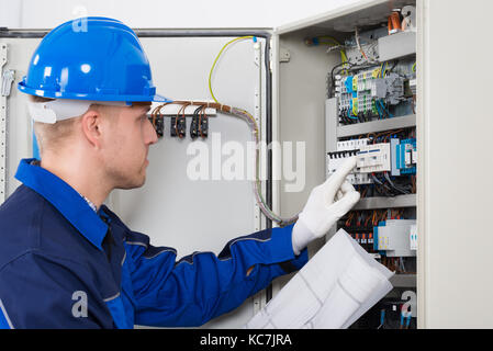 Male Electrician Testing Fusebox With Blueprint In Hand Stock Photo