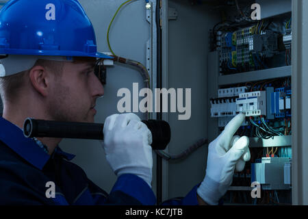 Male Technician Looking At Fusebox With Flashlight Stock Photo