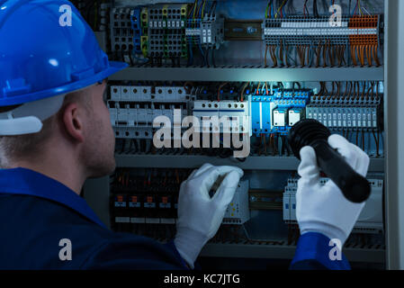 Male Technician Looking At Fusebox With Flashlight Stock Photo