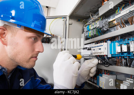 Male Electrician Working On Fusebox With Screwdriver Stock Photo