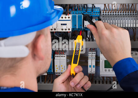 Male Electrician Examining Fusebox With Voltage Tester Stock Photo