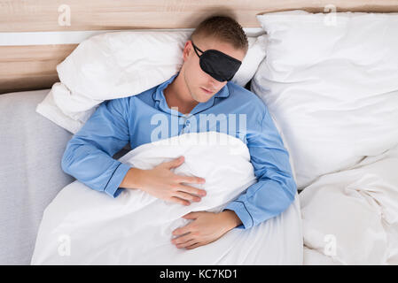 Young Man Wearing Eyemask While Sleeping On Bed Stock Photo