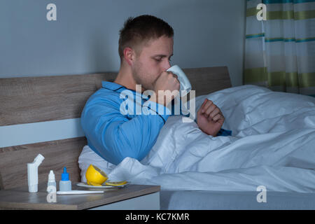 Young Man Sitting On Bed Holding Cup Of Coffee In His Bedroom Stock Photo