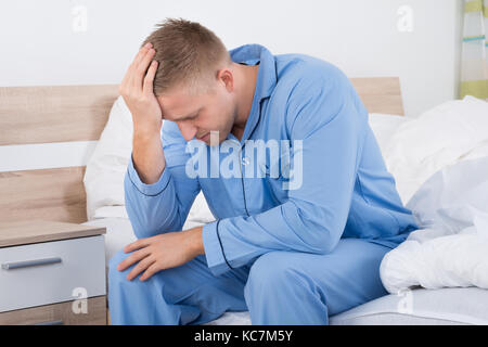 Young Woman Suffering From Headache Sitting On Bed Stock Photo
