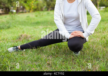 Young female warming up before workout in the park outdoor, stretching leg muscles Stock Photo