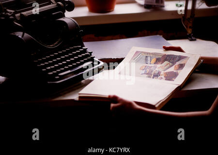 Old metal typewriter, covered in dust and rust. Hands with an old book on cooking .Retro Stock Photo
