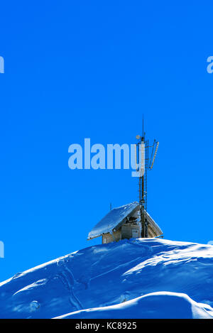 Small wooden cottage with communication antennas on top of a snow capped mountain Stock Photo