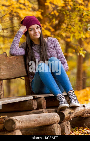 Teenage girl with sneakers seating on bench in autumn park Stock Photo