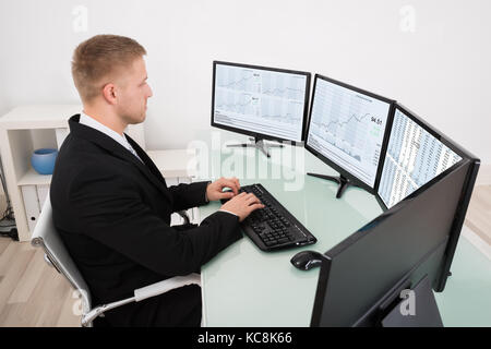 Young Businessman Looking At Graph On Multiple Computer Screen Stock Photo