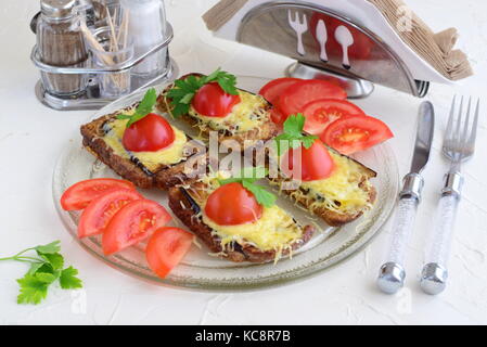 Toasts with aubergine, cheese and tomato on a glass plate on a white abstract background. Quick breakfast or snack. Stock Photo