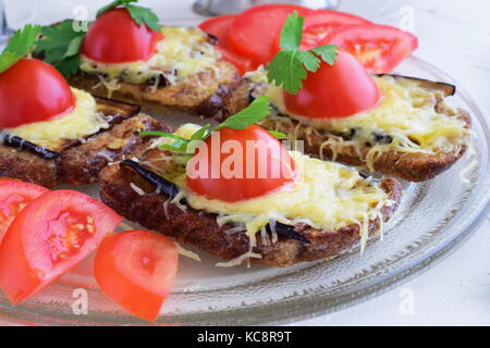 Toasts with aubergine, cheese and tomato on a glass plate on a white abstract background. Quick breakfast or snack. Stock Photo